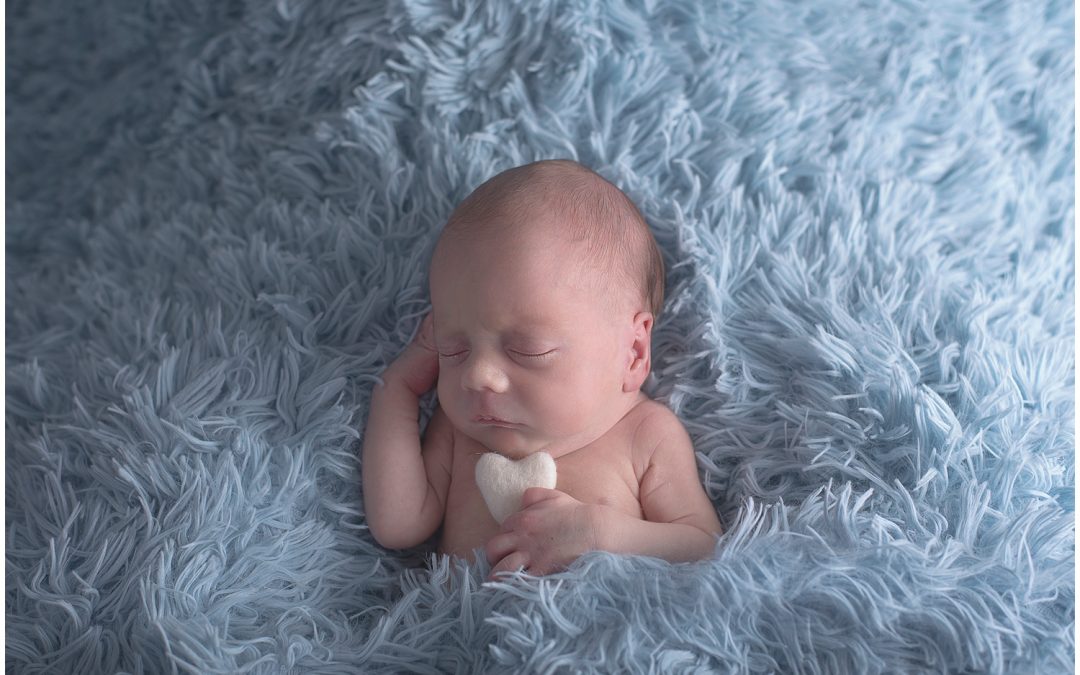 newborn on blue sheepskin holding felt heart